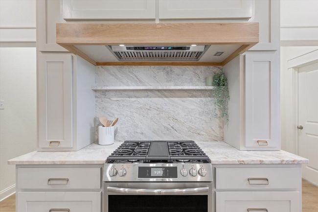 Kitchen featuring stainless steel gas stove, backsplash, light stone counters, white cabinets, and light wood-type flooring | Image 12