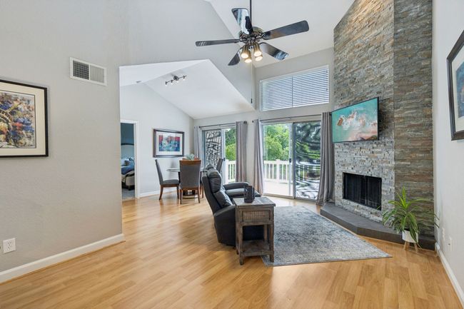Living room featuring high vaulted ceiling, baseboards, wood finished floors, a ceiling fan, and a fireplace | Image 8