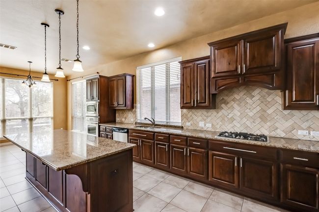 Kitchen featuring pendant lighting, a kitchen island, light stone countertops, appliances with stainless steel finishes, and visible vents | Image 15