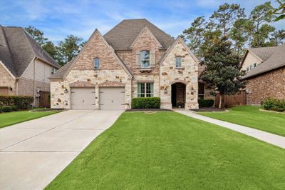 This is a spacious two-story brick & stone home featuring a double garage, arched entryway, and a well-manicured lawn, nestled in a residential neighborhood with tall trees. | Image 1