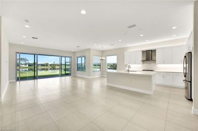 Kitchen with stainless steel fridge, wall chimney exhaust hood, a kitchen island with sink, and plenty of natural light. Also views of Dining, Breakfast area, and Living Room | Image 1