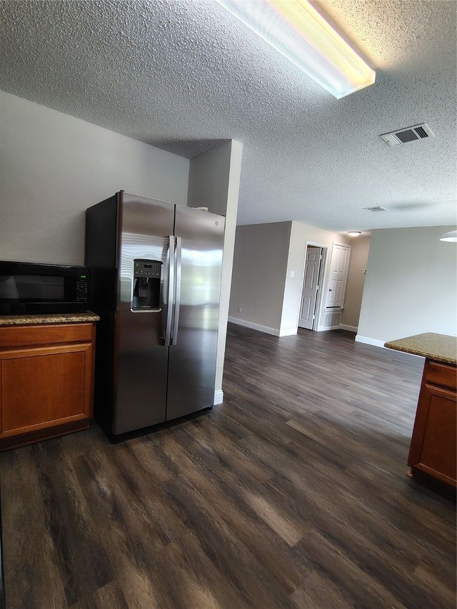Kitchen featuring stainless steel fridge, dark wood-type flooring, a textured ceiling, brown cabinetry, and open floor plan | Image 21