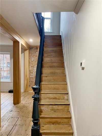 Staircase with ornamental molding, hardwood / wood-style flooring, and brick wall | Image 3