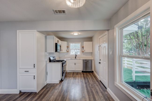 Kitchen with appliances with stainless steel finishes, dark wood finished floors, white cabinetry, a sink, and open shelves | Image 4