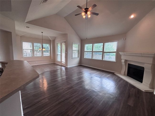 Unfurnished living room featuring ceiling fan, plenty of natural light, dark wood finished floors, a fireplace with raised hearth, and vaulted ceiling | Image 13