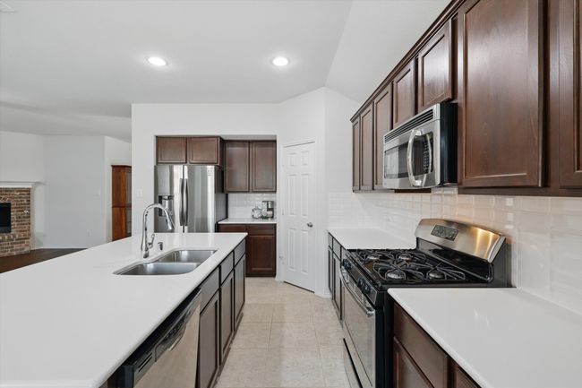 Kitchen featuring stainless steel appliances, a sink, dark brown cabinets, decorative backsplash, and light countertops | Image 26
