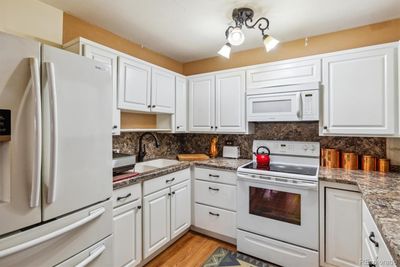 Kitchen features white cabinets, updated countertops and fixtures, and white appliances | Image 1