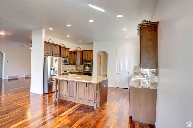 Kitchen with appliances with stainless steel finishes, light stone counters, ceiling fan, arched walkways, and decorative backsplash | Image 19