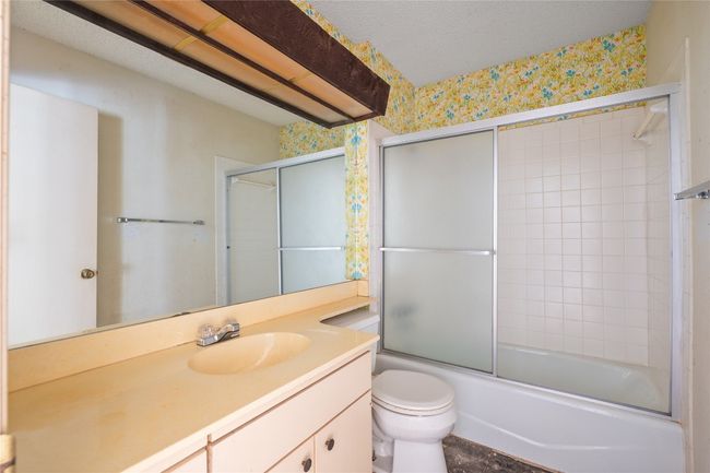 Full bathroom with wallpapered walls, vanity, and shower / bath combination with glass door | Image 10