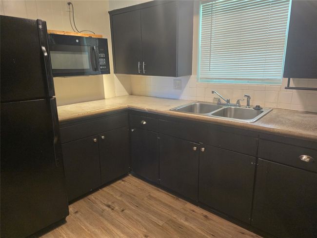 Kitchen with black appliances, light wood-style flooring, light countertops, and tasteful backsplash | Image 7