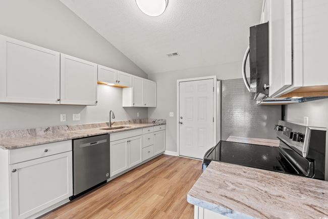 Kitchen featuring appliances with stainless steel finishes, vaulted ceiling, white cabinets, light wood-style floors, and a textured ceiling | Image 12