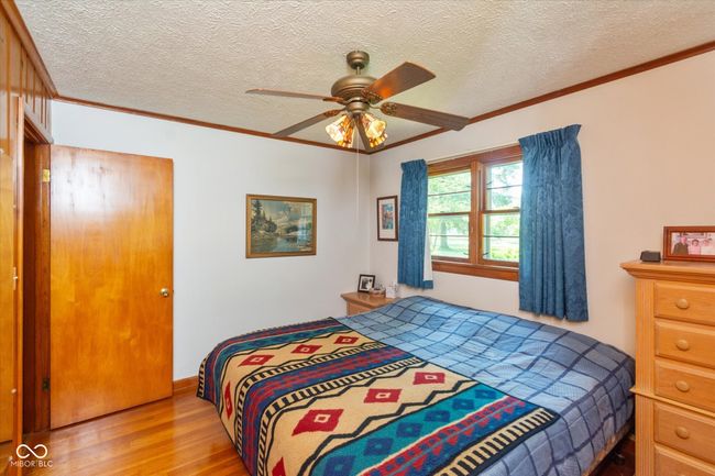 bedroom featuring wood finished floors, crown molding, a textured ceiling, and ceiling fan | Image 16