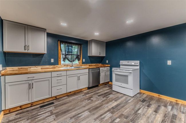 Kitchen featuring wooden counters, white electric range oven, a sink, stainless steel dishwasher, and wood finished floors | Image 9