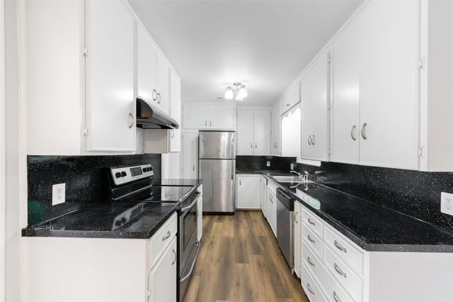 Kitchen featuring stainless steel appliances, under cabinet range hood, white cabinetry, dark wood-style floors, and decorative backsplash | Image 12