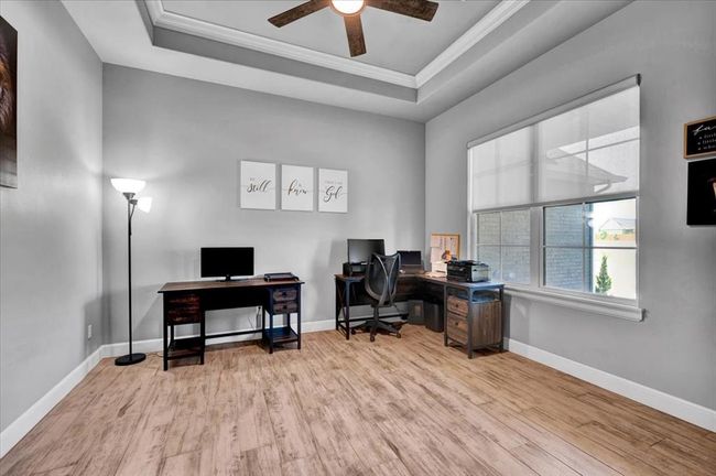 Office featuring light wood finished floors, a raised ceiling, a ceiling fan, ornamental molding, and baseboards | Image 12