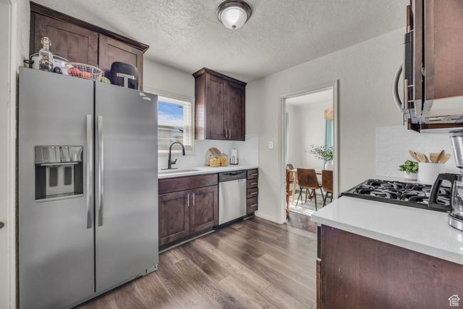 Kitchen with stainless steel appliances, a sink, dark wood-type flooring, a textured ceiling, and light countertops | Image 9