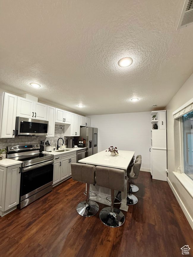 Kitchen with stainless steel appliances, a textured ceiling, light countertops, dark wood-type flooring, and tasteful backsplash | Image 4