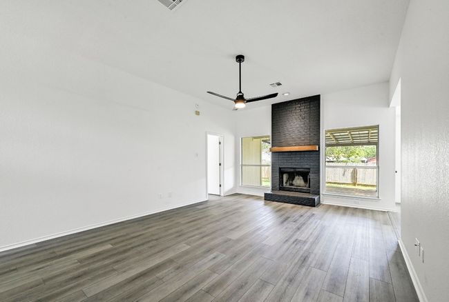 Unfurnished living room with dark wood-style flooring, a ceiling fan, and a brick fireplace | Image 8