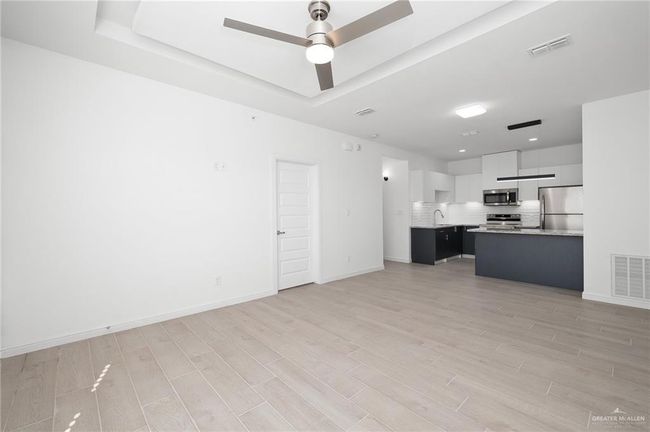 Unfurnished living room with light wood-style flooring, a ceiling fan, and a raised ceiling | Image 4
