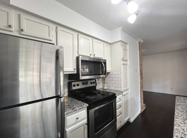 Kitchen featuring light stone counters, backsplash, baseboards, appliances with stainless steel finishes, and dark wood-type flooring | Image 7
