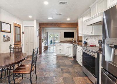 Kitchen with white cabinets, dark tile patterned flooring, appliances with stainless steel finishes, kitchen peninsula, and decorative backsplash | Image 3