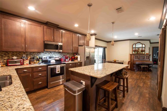 Kitchen featuring stainless steel appliances, ornamental molding, decorative backsplash, a kitchen breakfast bar, and a center island | Image 10
