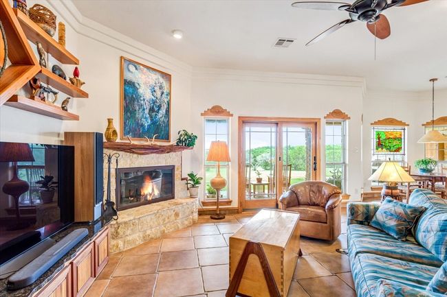 Living area with plenty of natural light, a glass covered fireplace, ceiling fan, light tile patterned floors, and crown molding | Image 10