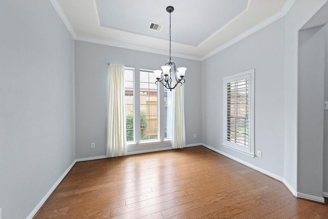 The dining room is bright and airy, featuring rich hardwood flooring, chandelier, and large windows with plantation shutters that let in abundant natural light. | Image 7