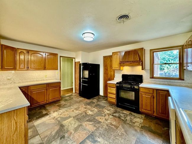 Kitchen featuring black appliances, premium range hood, brown cabinetry, and light countertops | Image 9