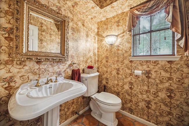 Elegant vintage wallpaper and a classic pedestal sink with brass fixtures. A decorative mirror and soft window drapes add charm, while the salitto floor complements the warm tones. | Image 14
