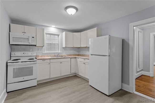 Kitchen with tasteful backsplash, white appliances, light countertops, light wood finished floors, and a sink | Image 12