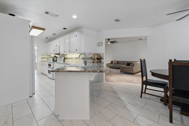 Kitchen featuring white appliances, a ceiling fan, light marble finish floors, a peninsula, and white cabinetry | Image 11