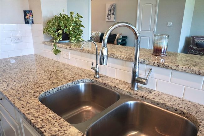 Kitchen view of a sink, tasteful backsplash, light stone countertops, and white cabinets | Image 7