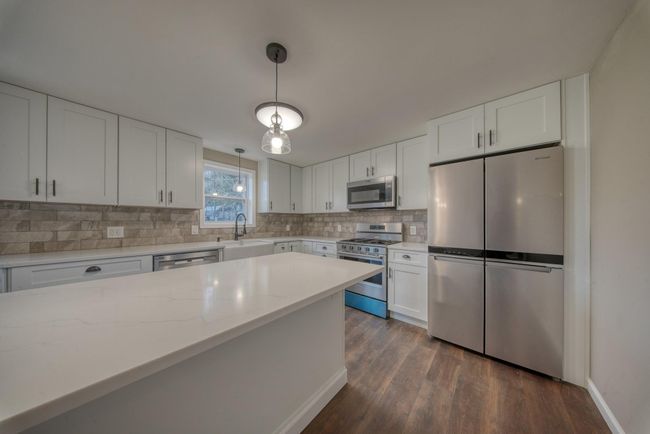 Kitchen featuring white cabinets, a sink, decorative light fixtures, decorative backsplash, and appliances with stainless steel finishes | Image 10