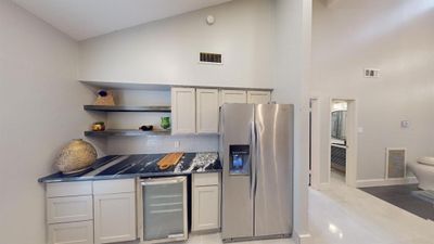 View of kitchen with built-in beverage cabinet , refrigerator and floating shelves with extra cabinet area and built in spice rack in the pantry area. | Image 3