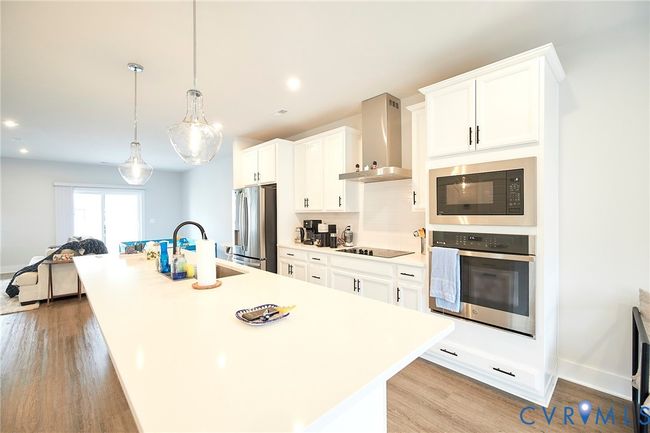 Kitchen featuring black appliances, a center island with sink, wall chimney exhaust hood, white cabinets, and recessed lighting | Image 41