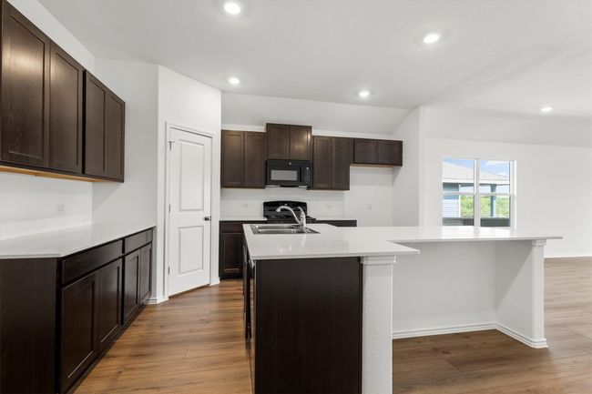 Kitchen featuring black microwave, a center island with sink, dark wood finished floors, recessed lighting, and light countertops | Image 5