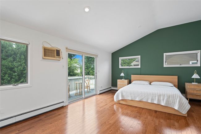 Bedroom featuring vaulted ceiling, access to exterior, wood finished floors, a baseboard radiator, and two closets | Image 22