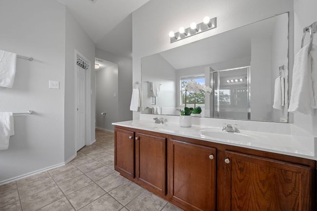 Full bath with double vanity, a shower stall, tile patterned floors, baseboards, and vaulted ceiling | Image 20