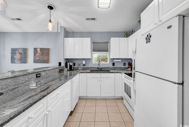 Kitchen with white appliances, a textured ceiling, white cabinetry, dark stone counters, and hanging light fixtures | Image 20