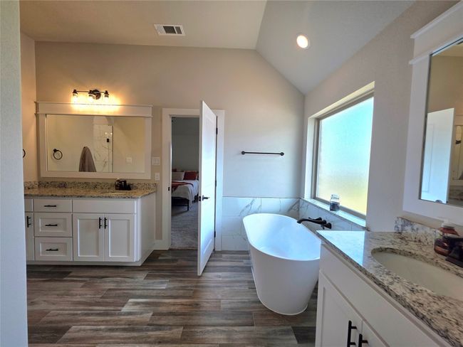 Ensuite bathroom with lofted ceiling, tile walls, two vanities, a soaking tub, and wood finished floors | Image 22