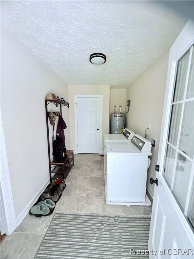 Laundry featuring washer and dryer, a textured ceiling, baseboards, and water heater. Closet for storage also | Image 11