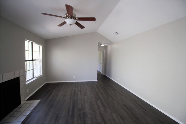 Unfurnished living room with dark wood finished floors, ceiling fan, vaulted ceiling, and a tile fireplace | Image 6