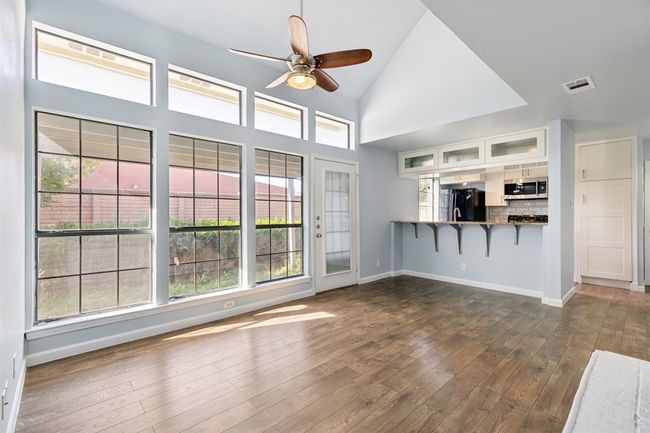 Unfurnished living room featuring baseboards, visible vents, wood finished floors, ceiling fan, and high vaulted ceiling | Image 6