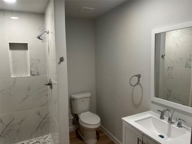 Bathroom with a tile shower, wood finished floors, visible vents, toilet, and vanity | Image 35