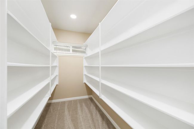 With white shelving on both sides, carpeted flooring, and neutral walls, this walk-in pantry offers organized and accessible storage. | Image 35