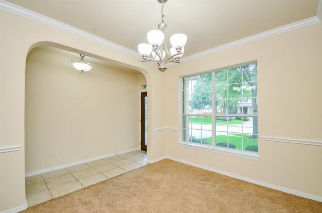 A bright dining area with large windows offering plenty of natural light. It features a modern chandelier, neutral-colored walls, and a mix of carpet and tile flooring. The space is open and inviting, ideal for gatherings. | Image 6