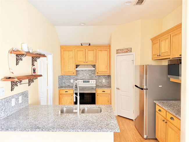Kitchen with appliances with stainless steel finishes, under cabinet range hood, light brown cabinetry, light wood-style flooring, and lofted ceiling | Image 15
