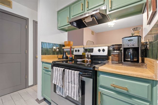 Kitchen with electric range, visible vents, green cabinets, under cabinet range hood, and light tile patterned flooring | Image 21