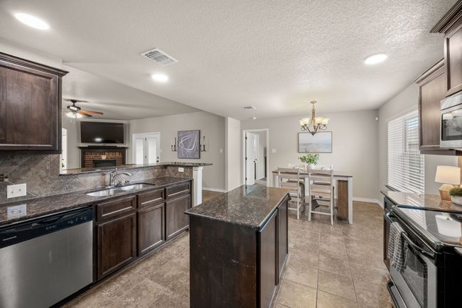 Kitchen with stainless steel dishwasher, electric stove, ceiling fan, dark brown cabinets, and dark stone countertops | Image 12